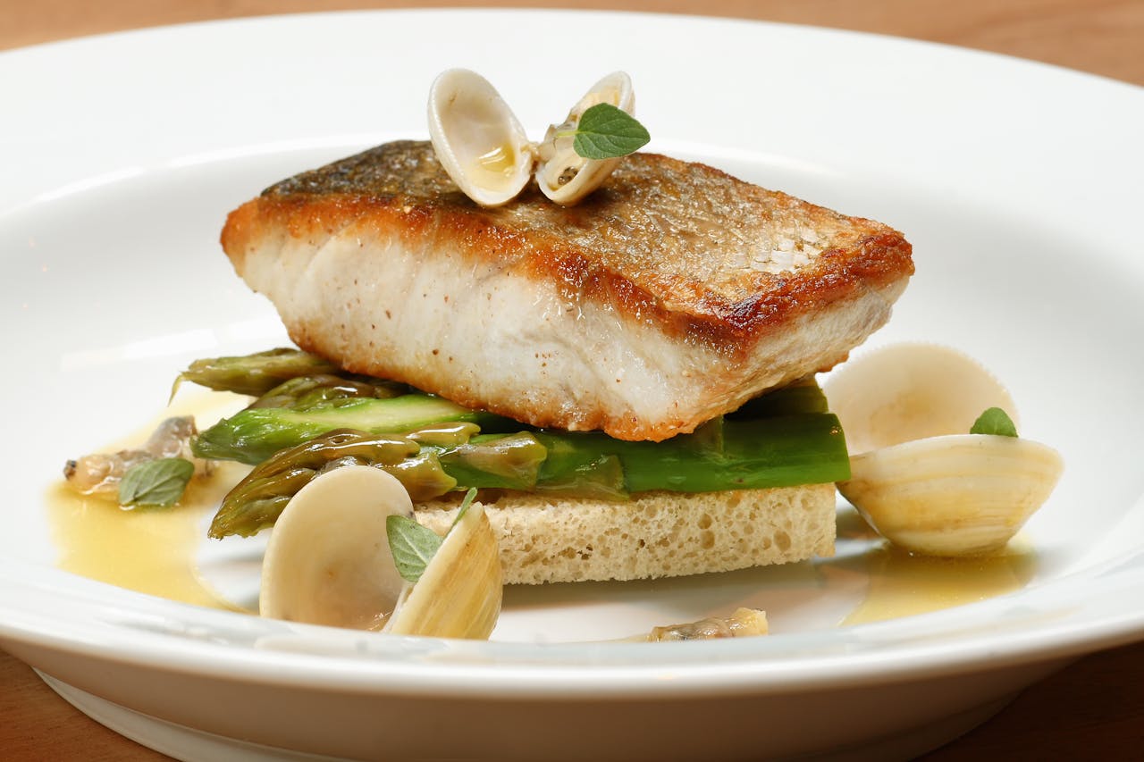 A gourmet fish dish served with clams and asparagus on a white plate.