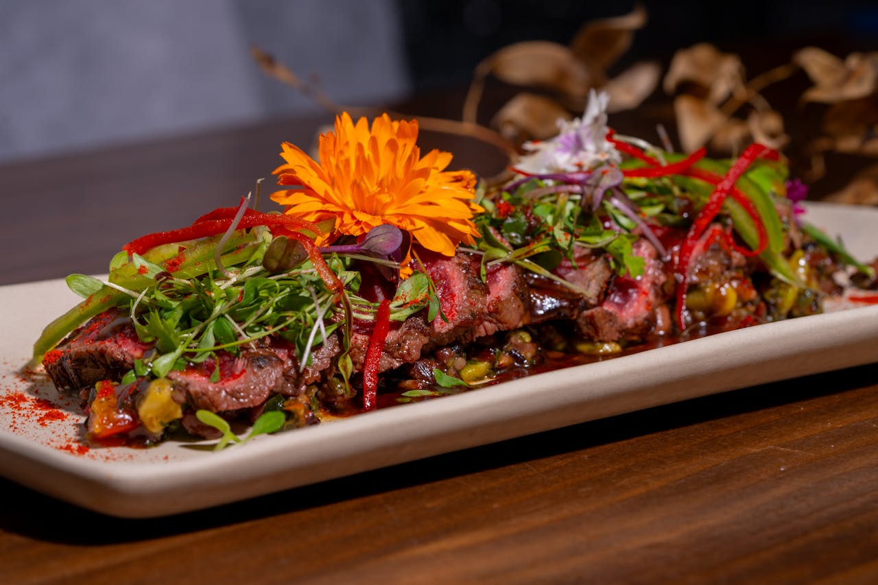 Sliced gourmet steak garnished with microgreens and vibrant edible flowers on a plate.